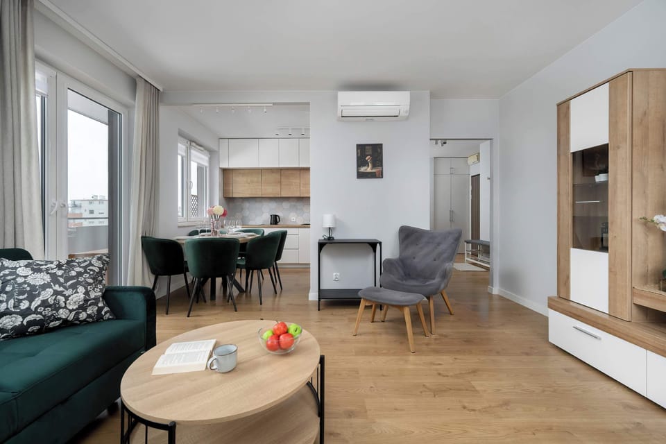 A dining arrangement for four featuring neatly stacked plates, elegant cutlery, and glasses. The warm wood of the table contrasts beautifully with the dark green chairs. The table setting feels prepared for a cozy meal.