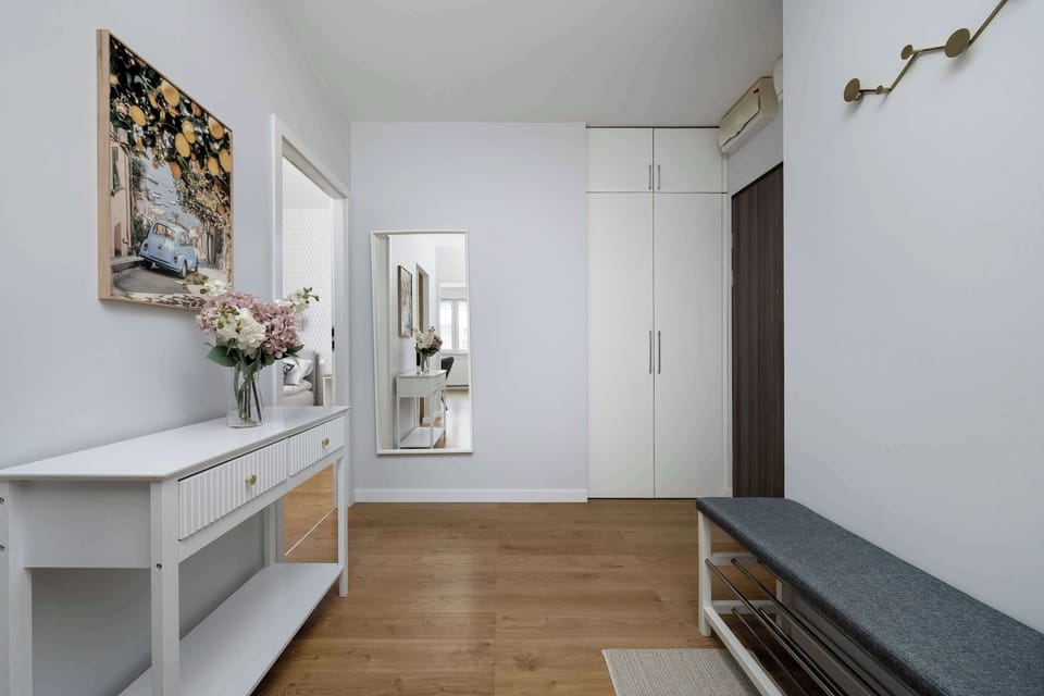 A hallway leading toward the living space with bright lighting and mirrors along the walls. Wooden flooring ties the space together. Artwork adds charm to the transition area.