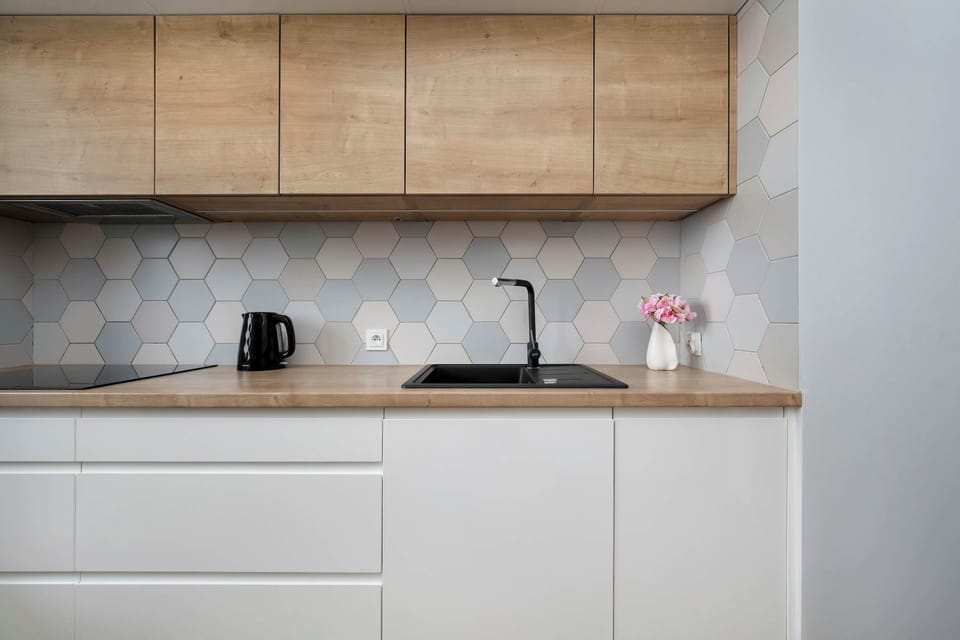 A compact kitchen corner with white cabinetry and wooden upper cabinets. A kettle and other small appliances sit neatly on the counter. The clean minimalist design enhances the space.