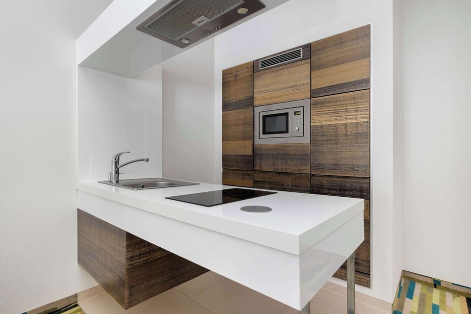 A compact kitchen with white countertops, built-in appliances, and a simple modern backsplash.