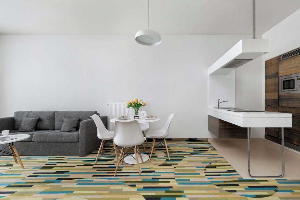 A living room with a gray sectional placed on a multicolored rug, facing a small dining table.