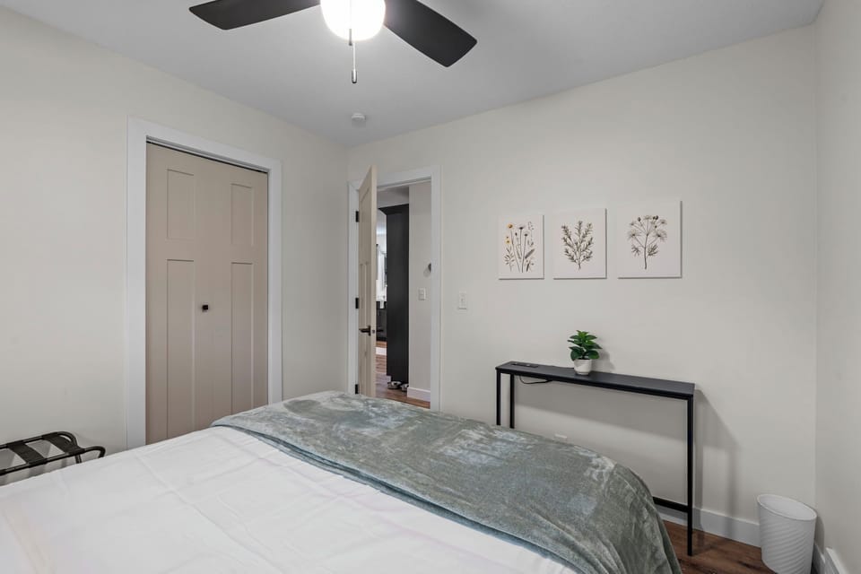 Unwind in your peaceful bedroom featuring botanical artwork, a ceiling fan for comfort, and thoughtful touches like a bedside plant to help you relax.