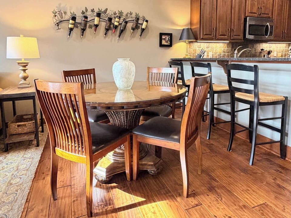 Sunlit dining area with carved pedestal table, seating for four, and wall-mounted wine rack — pour a glass before you even unpack
