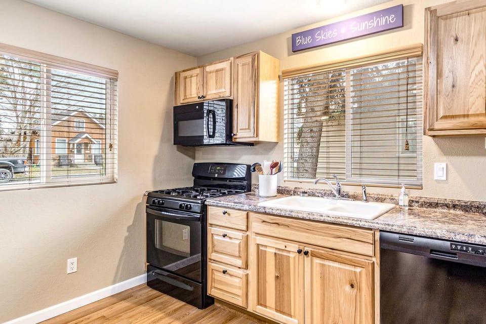 Sunny kitchen corner with gas range, granite-look counters, window sink, and neighborhood view