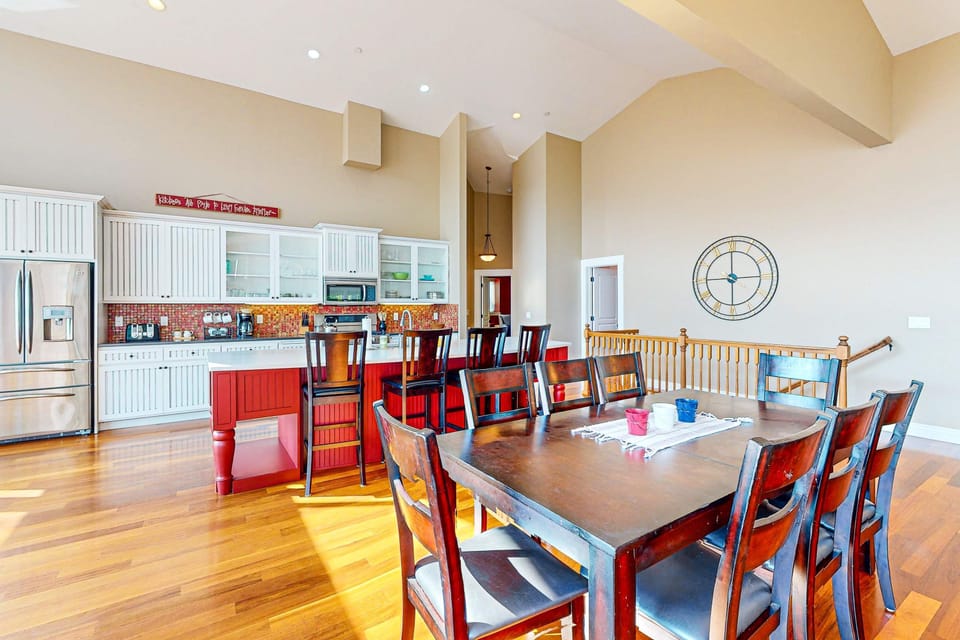 Sunlit open-plan dining and kitchen with 8-seat dining table, vaulted ceilings, and kitchen island — where the whole group gathers after a day on the lake