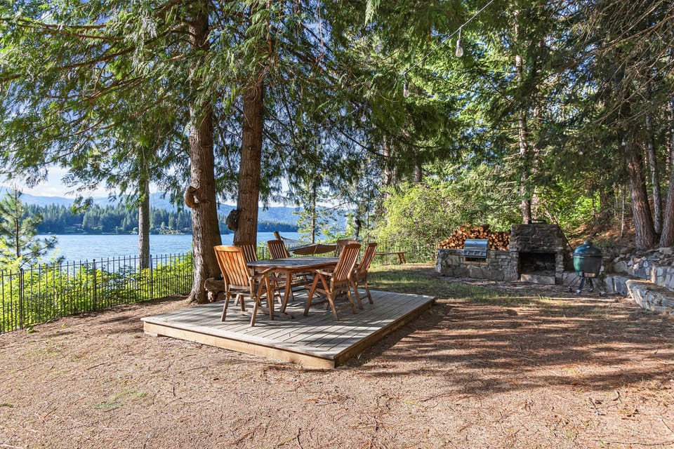 Sunlit lakefront area with dining table, charcoal, and gas grill — dinner with a mountain-lake backdrop