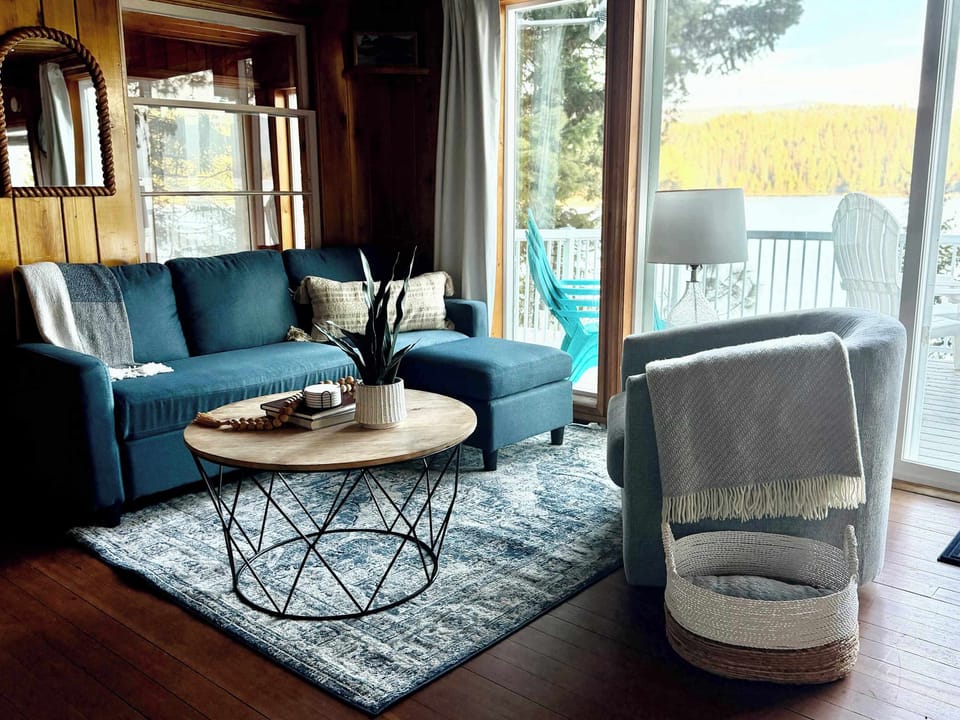 Living room with teal sectional, accent armchair with throw blanket & bright lakefront sliding door — cozy cabin charm with the lake always in sight