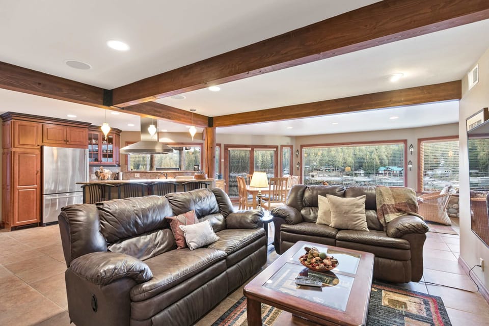 Bright open-plan living room with leather sofas, wood beams, and panoramic water-view windows