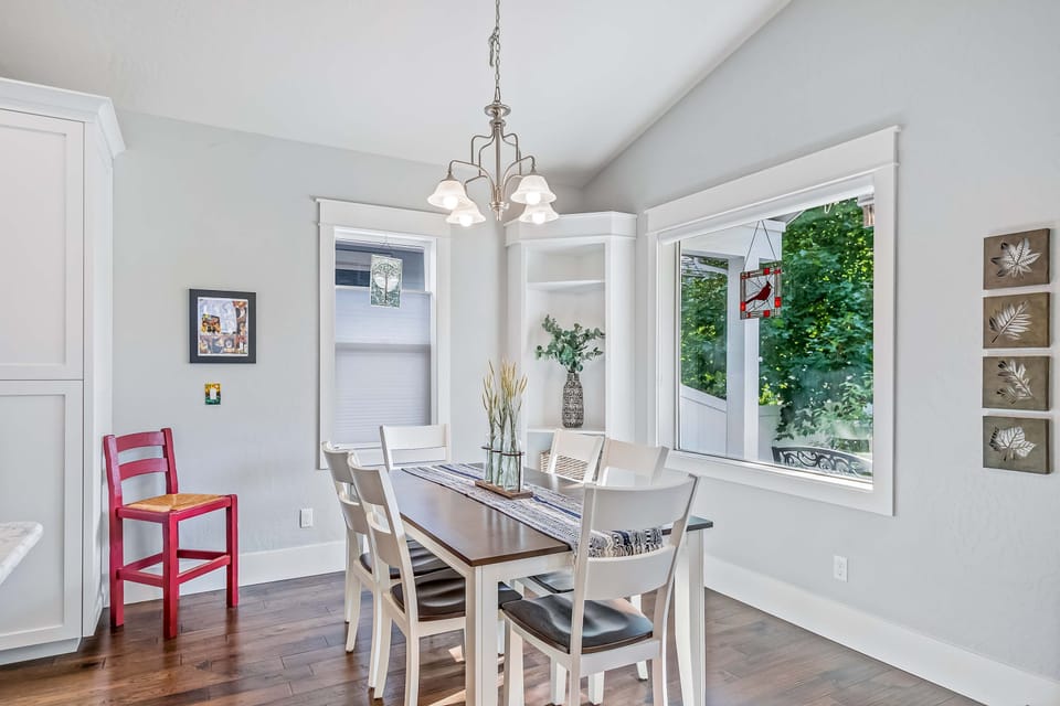 Bright dining nook with chandelier, garden-view corner windows, and seating for six — morning light and tree views over every breakfast
