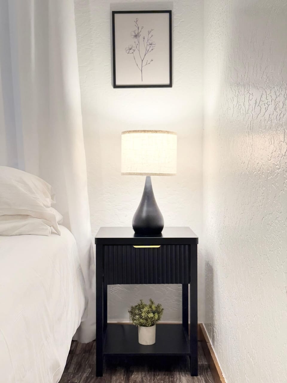 Bedroom detail — ribbed black nightstand with ceramic lamp and botanical art, warm and thoughtfully styled