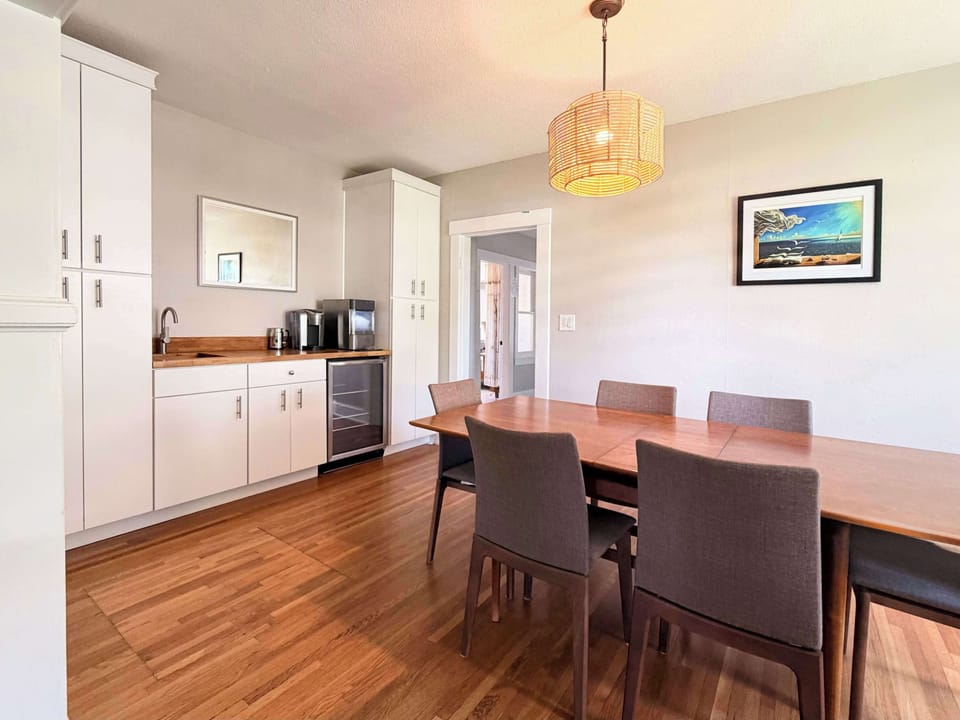 Bright dining room with six-seat wood table, rattan pendant, and open archway to living room — plenty of space for the whole group to gather