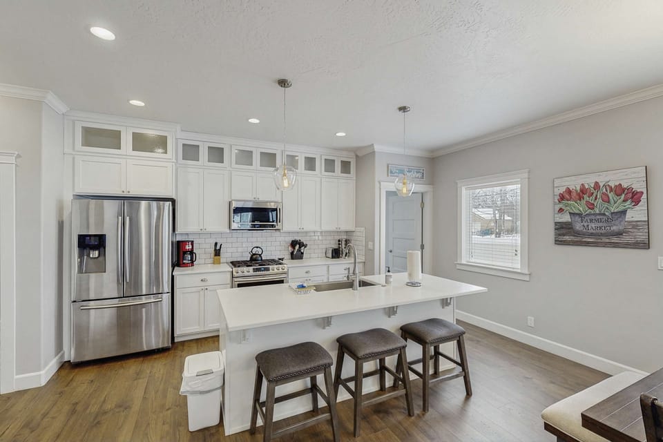 Bright white kitchen with stainless appliances, gas range, island with 3-stool bar seating, pendant lights
