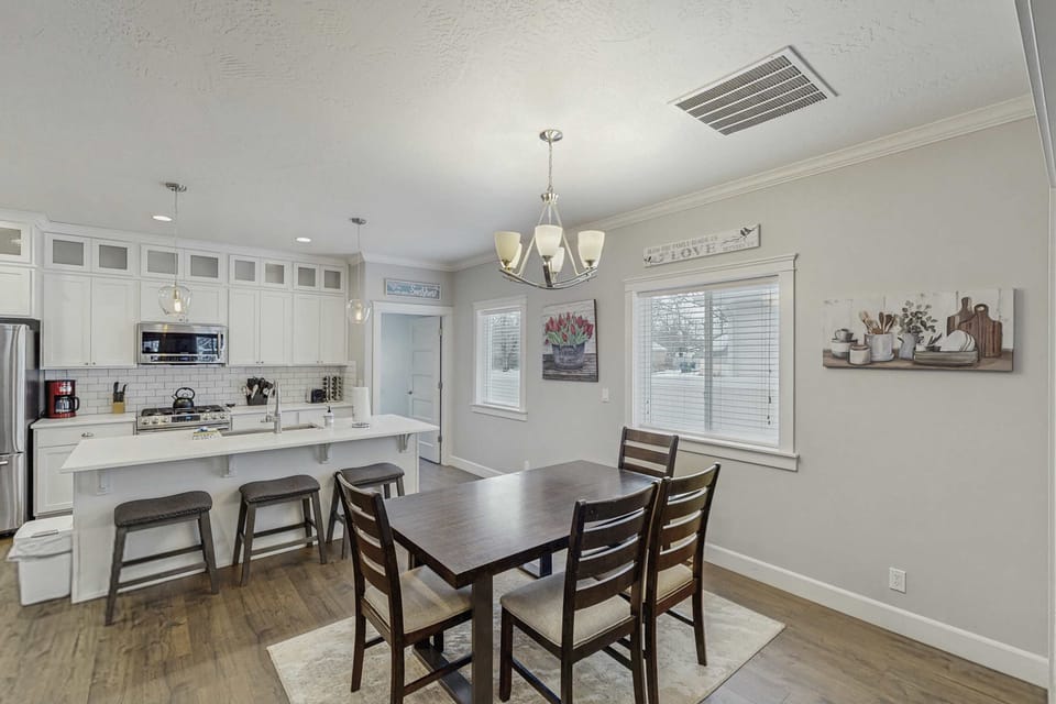 Dining area with 4-seat table and chandelier, open to white-cabinet kitchen with island bar seating