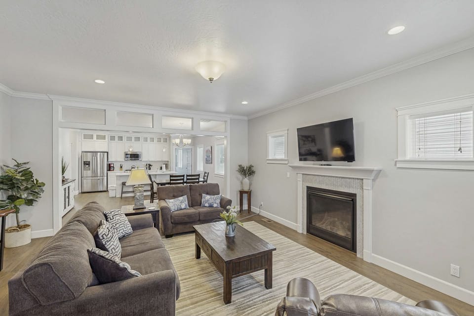 Bright open-plan living room with fireplace, wall-mounted TV, and view into kitchen and dining