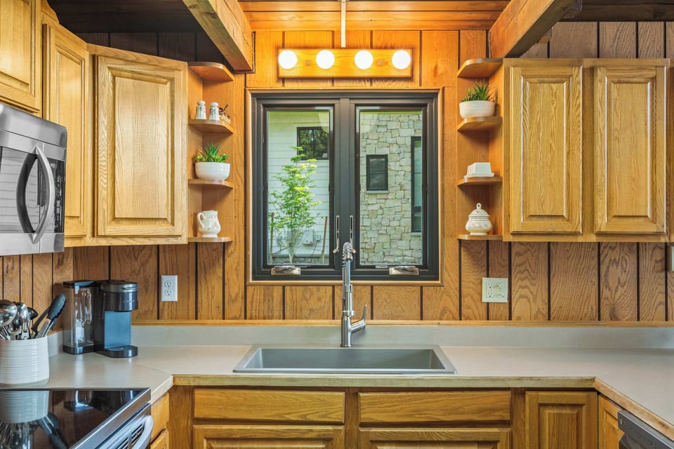 Kitchen sink station with garden window, open display shelves, Keurig, and wood-paneled surround — bright and ready for morning coffee rituals