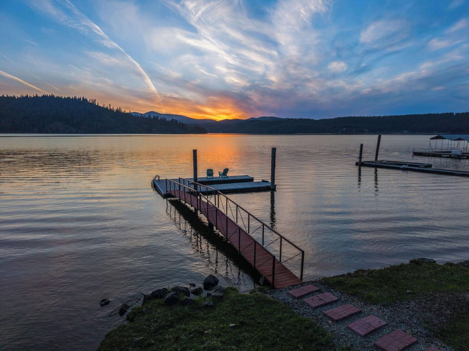 Twilight private dock with railed walkway, Adirondack chairs & glowing lake-mountain sunset — the view that sells itself