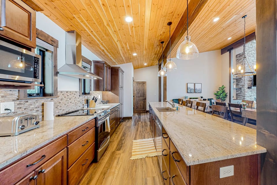 Bright full kitchen with granite island, stone tile backsplash, stainless appliances, and open sightline to dining area