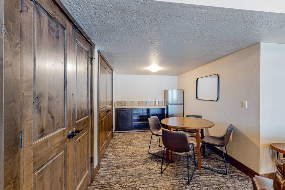 Lower-level bonus room with kitchenette, round dining table for 4, and tall knotty-wood storage doors