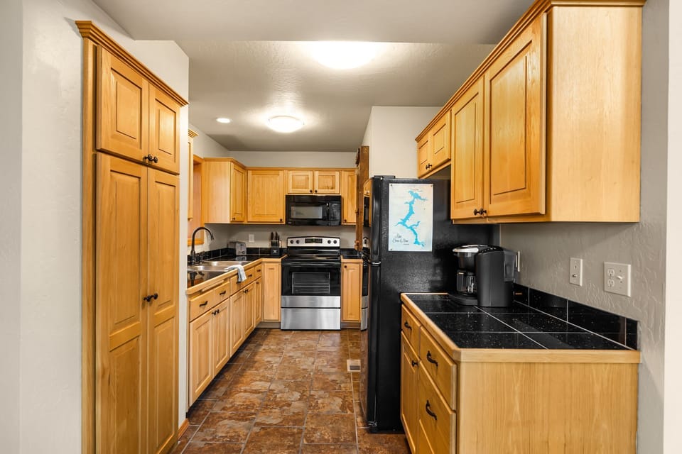 Full kitchen with warm wood cabinetry, dark tile counters, stainless range, and tall pantry cabinet — everything needed for a real cabin meal.