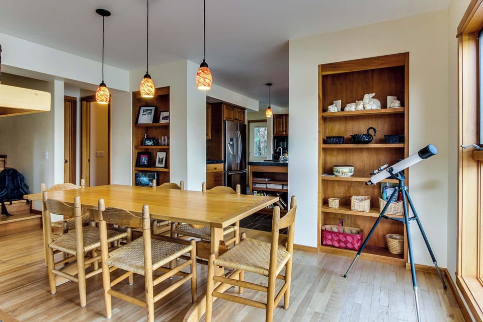 Sunlit dining area seats six under pendant lights, built-in shelving, and a telescope ready for stargazing on Hayden Lake