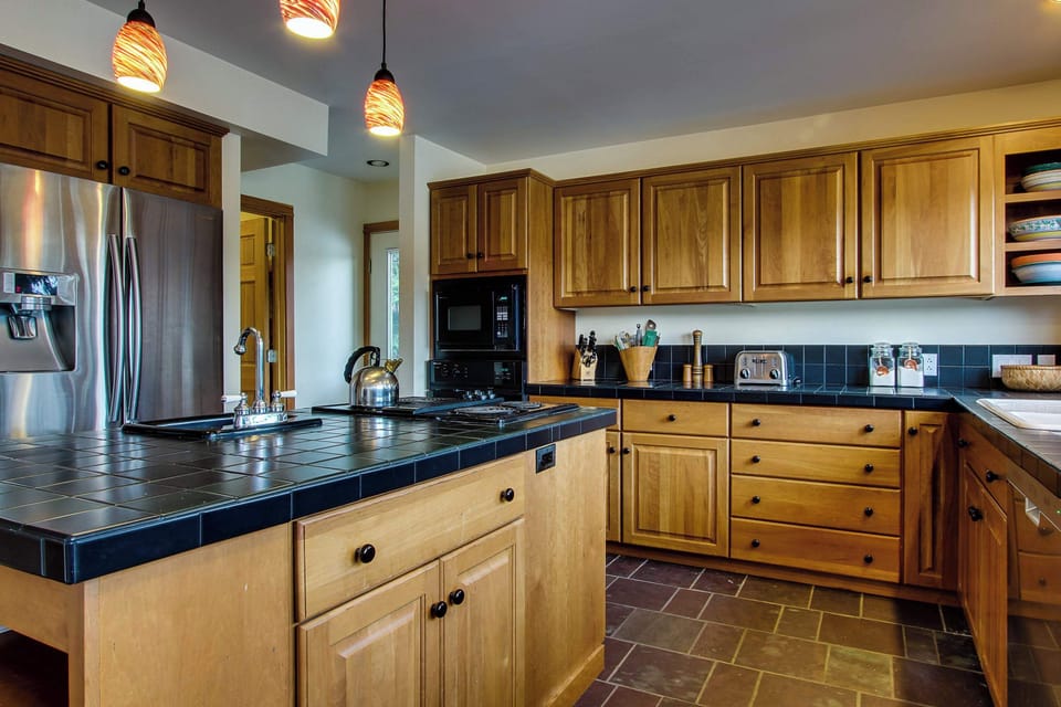 Kitchen close-up: island cooktop, dark tile counters, warm wood cabinetry, and ample storage for cooking big group meals