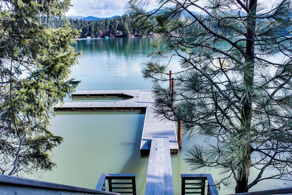 Elevated view of the private L-shaped dock framed by lakeside pines — turquoise-green water and forested hills stretching to the horizon