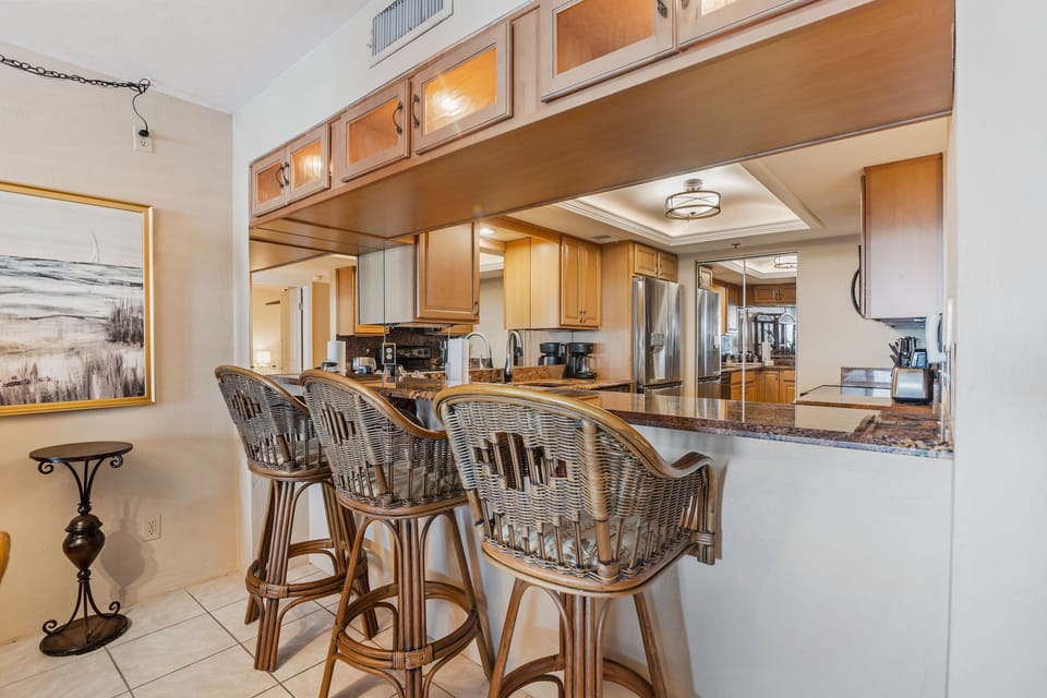 Fully equipped coastal kitchen with granite countertops and wicker bar seating, perfect for casual meals after a day at the beach. Ideal for relaxed beach stays with comfort, style, and easy entertaining.