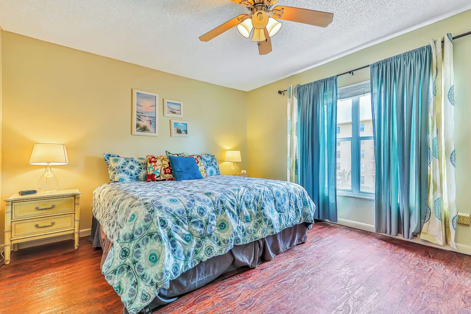 Unwind after a fun-filled beach stay in this serene bedroom featuring a comfortable bed, coastal décor, ceiling fan, and natural light—your perfect retreat for rest and relaxation by the shore.