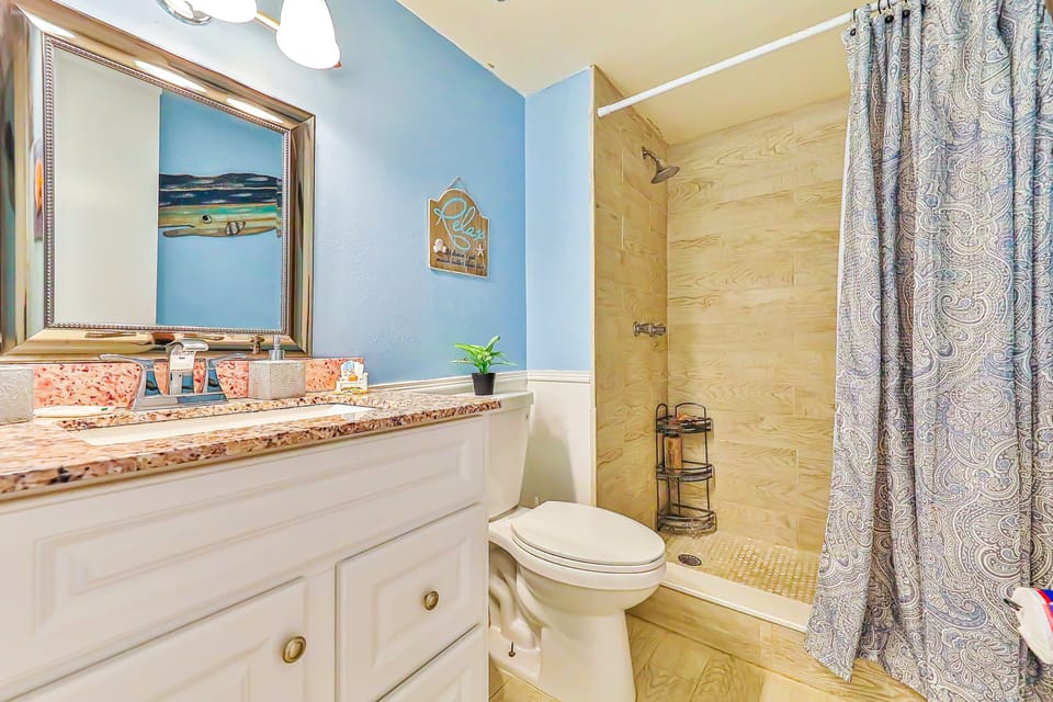 Refresh during your beach stay in this bright bathroom featuring a granite vanity, walk-in shower, and coastal accents—perfect for rinsing off after a day of sun, sand, and surf.