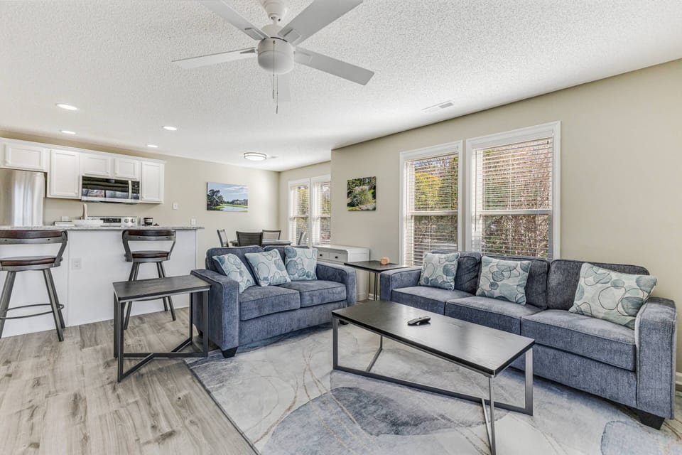 The living room is located next to the kitchen and dining area, which features a breakfast bar with seating for two.