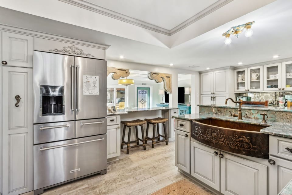 Updated Kitchen Featuring Granite Countertops, Double Ovens, an Oversized Refrigerator, a Large Farmhouse Style Sink, Barstool Seating for 4, and Charming Mermaid Design Touches