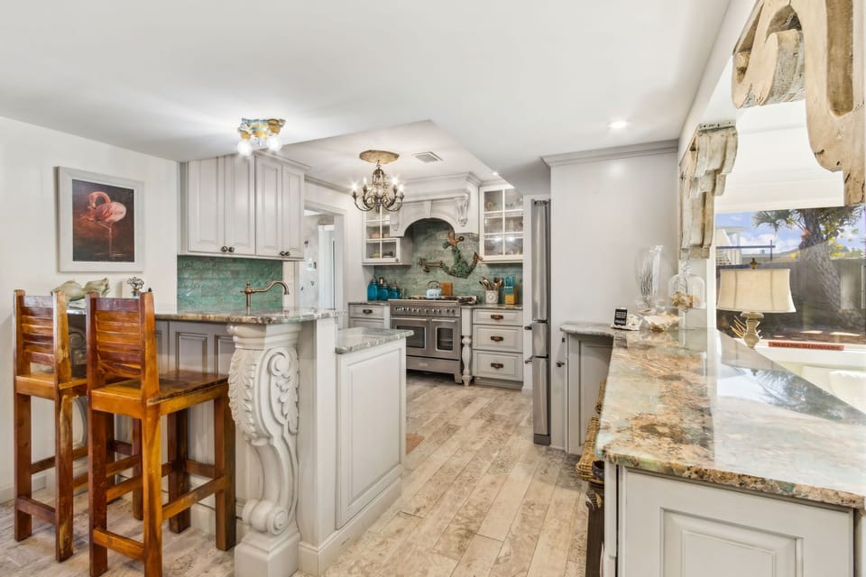 Updated Kitchen Featuring Granite Countertops, Double Ovens, an Oversized Refrigerator, a Large Farmhouse Style Sink, Barstool Seating for 4, and Charming Mermaid Design Touches