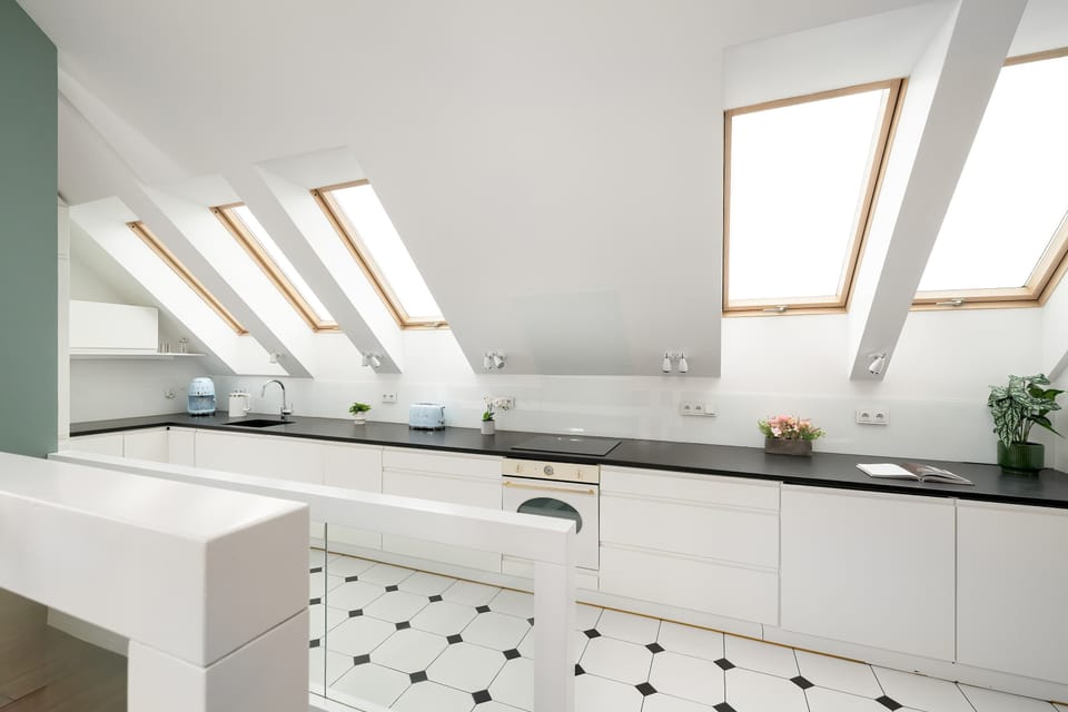 A bright kitchen with skylights illuminating glossy white countertops. The modern layout creates an open and airy feeling.