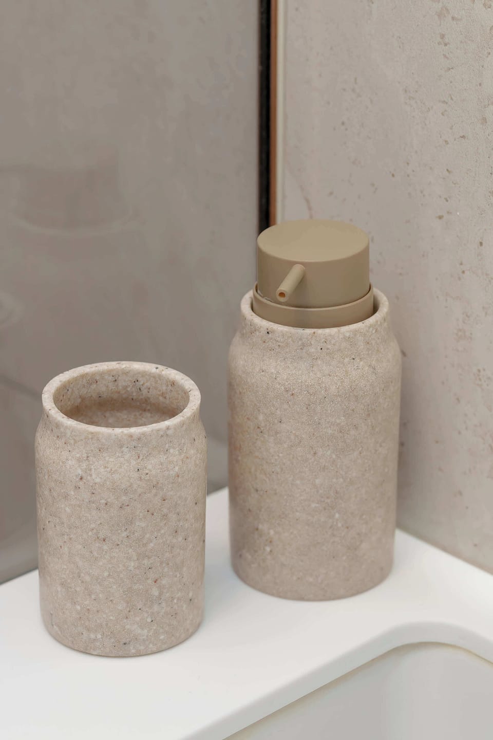 A close-up of earthy-toned bathroom accessories, such as ceramic jars and a soap dispenser. The matte textures and neutral hues create a calming aesthetic. They sit arranged on a clean countertop.