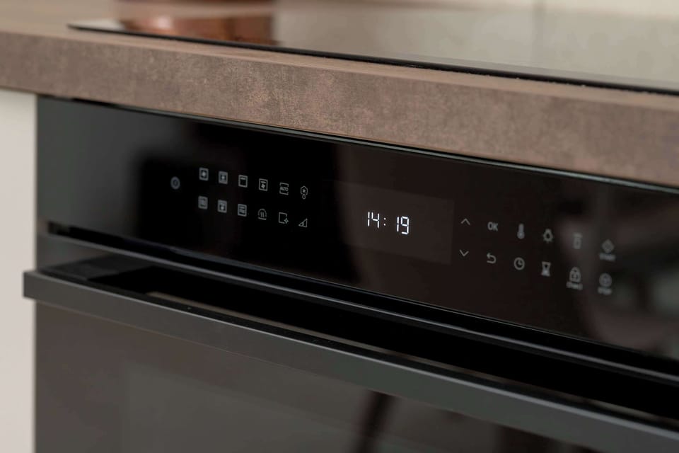 A close-up of a built-in oven with a digital control panel. The reflective surface of the appliance blends well with the sleek kitchen cabinetry. The dark finish contrasts nicely with the light countertops.