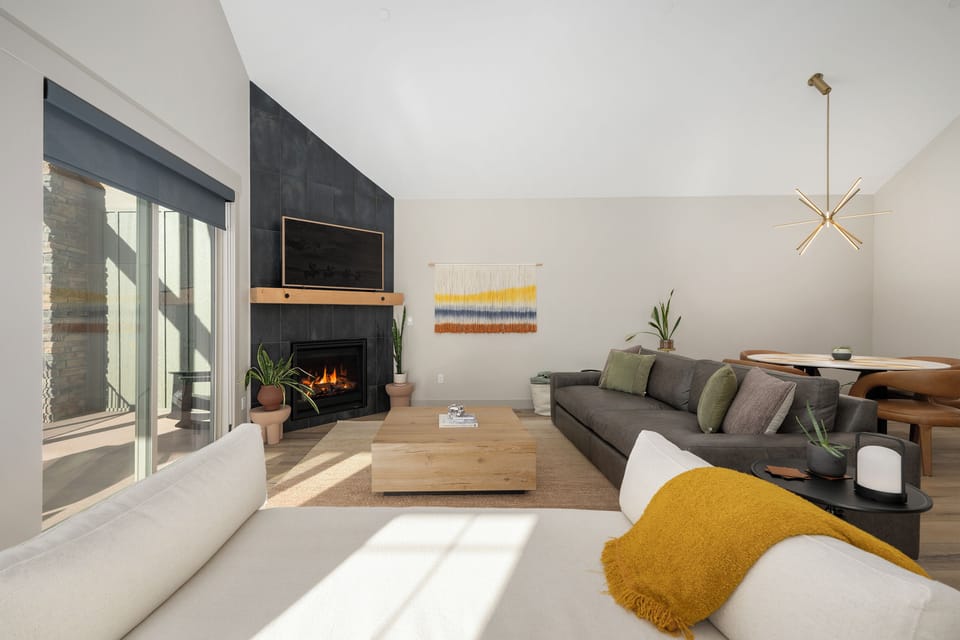 Sink into the plush sofa by your crackling fireplace, where natural light streams through floor-to-ceiling windows into this modern living space.