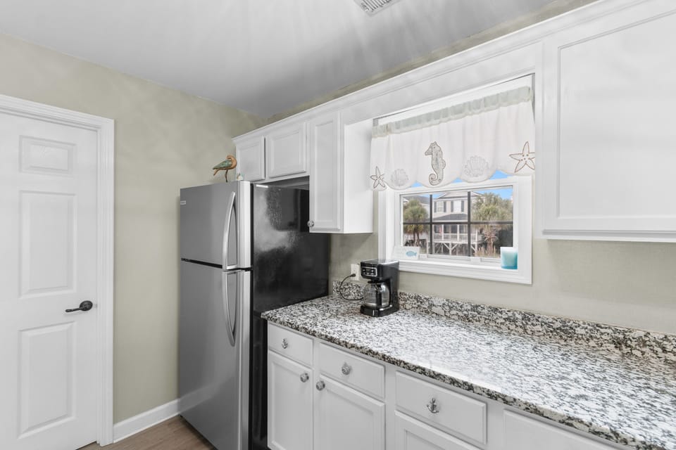 Your fully equipped kitchen features granite counters and stainless appliances, with charming coastal views through the window.