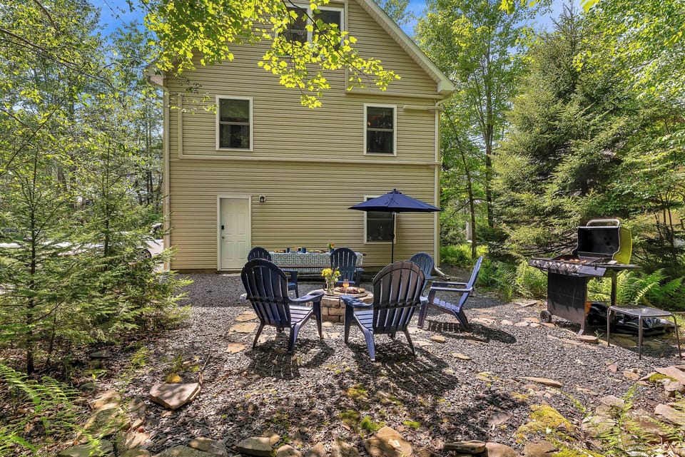 Tucked into the trees, the backyard retreat features a cozy fire pit with Adirondack chairs, a charcoal grill, a shaded dining area, and a hammock strung between the pines—perfect for lazy afternoons and starry nights.