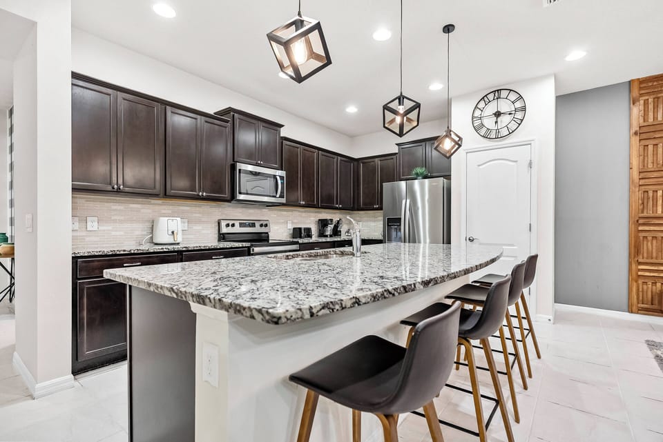 Experience the charm of this stylish kitchen featuring dark cabinets and light granite countertops. Modern pendant lights illuminate the space, while a spacious island invites you to enjoy casual dining and great conversations.