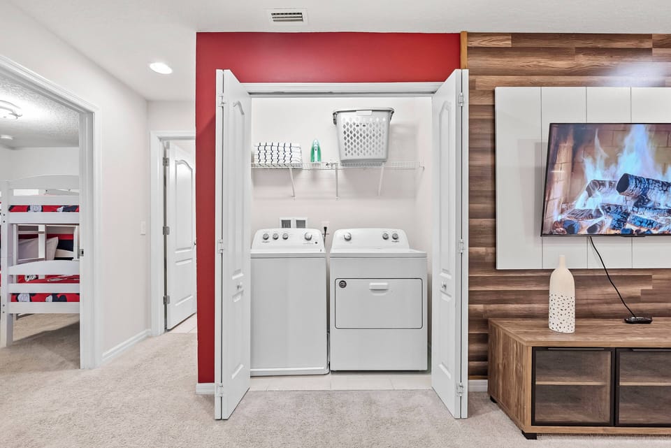 This well-designed laundry area offers sleek white appliances that harmonize with warm wood accents and a vibrant red wall, creating a convenient space for tackling chores during your stay while enjoying a homey atmosphere.
