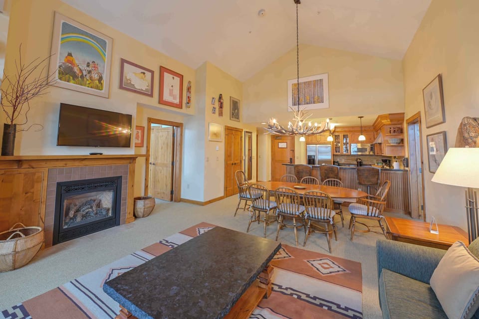 The open-concept living area features vaulted ceilings and a cozy fireplace, providing an inviting atmosphere adorned with colorful mountain-inspired artwork.