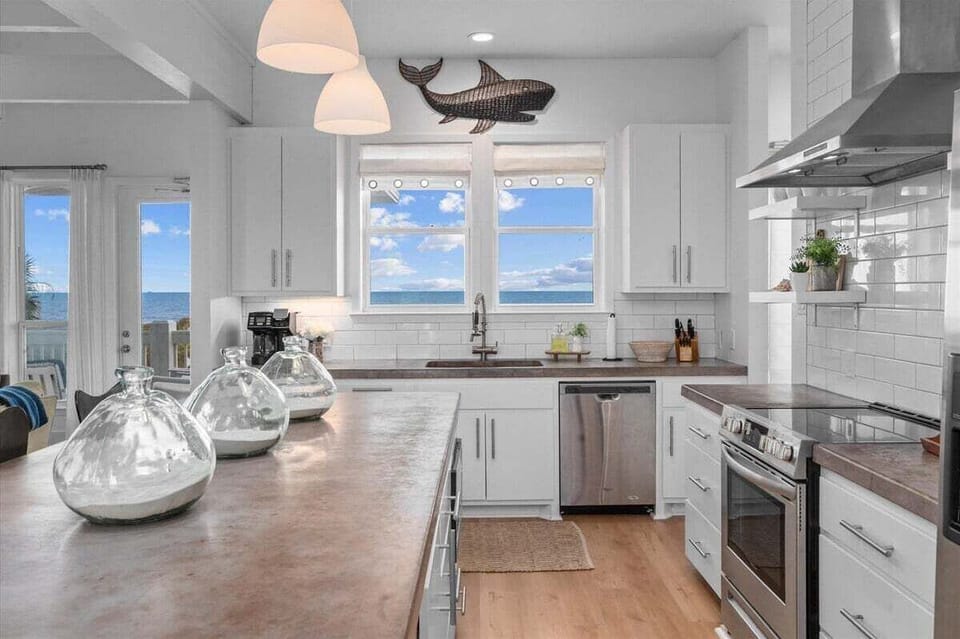 Modern kitchen with stainless steel appliances, large island, and ocean-facing windows – fully equipped vacation rental kitchen