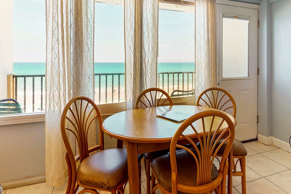 Enjoy meals in this bright ocean-view dining area featuring a cozy table and direct access to a beachfront balcony. Perfect for a relaxing beach stay with coastal views, sea breezes, and the shoreline just outside your door.
