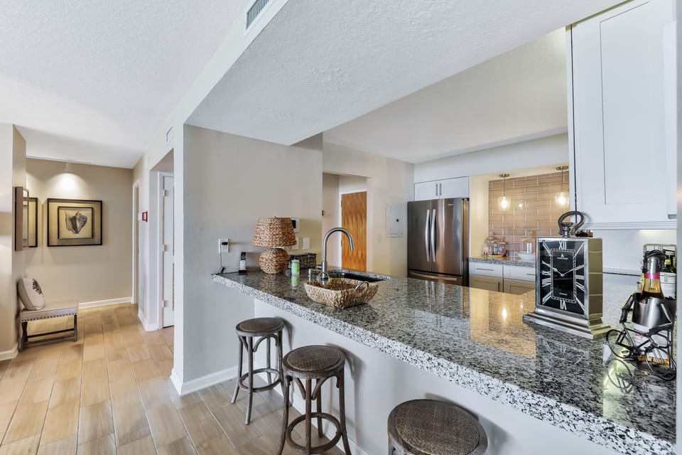 Stylish coastal kitchen featuring granite countertops, stainless appliances, and bar seating. Perfect for quick bites or gathering after a day of sun and relaxation during your beach stay.