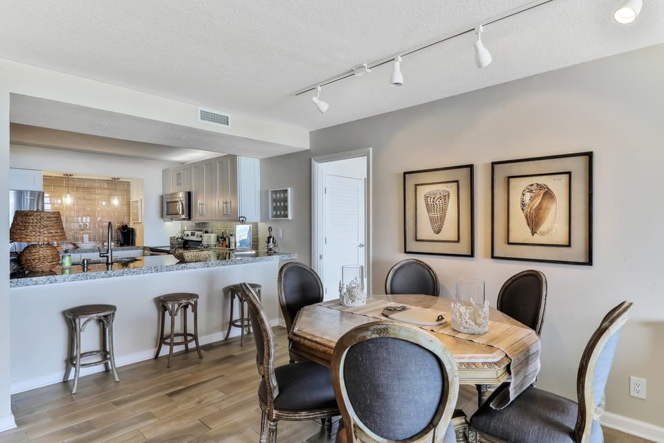 Charming coastal dining area with beach-inspired décor, seating for gathering, and an open kitchen with breakfast bar. Ideal for sharing meals and relaxing together during your beach stay.