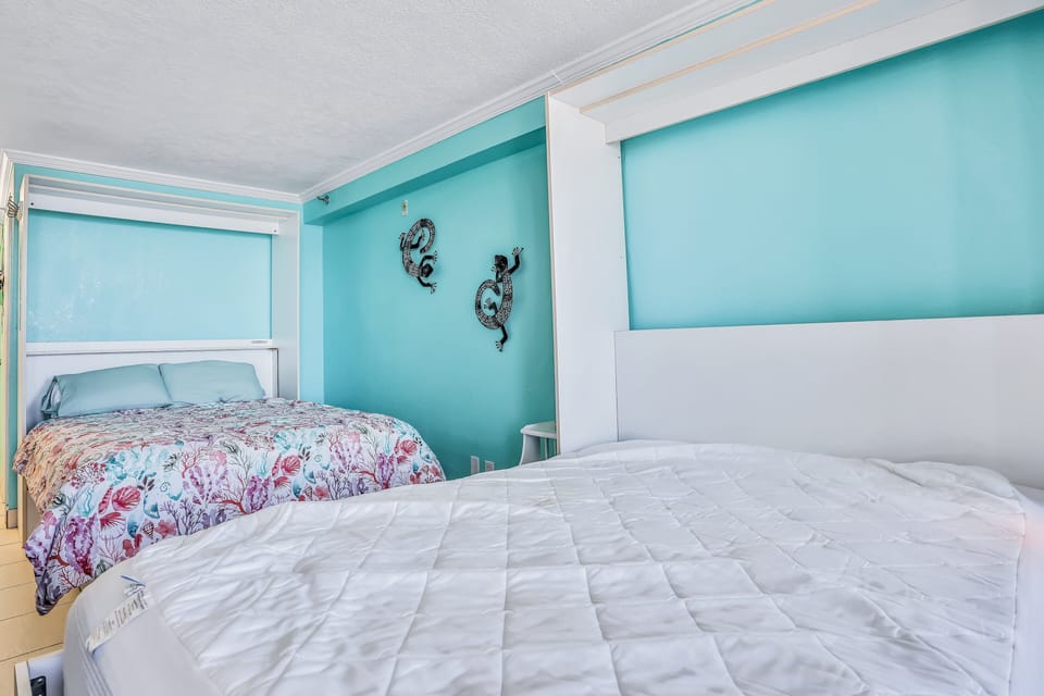 Versatile beach stay sleeping space featuring a Murphy bed and cozy coastal bedding. Perfect for families or groups, this bright beachfront retreat offers comfort and convenience just steps from the ocean.
