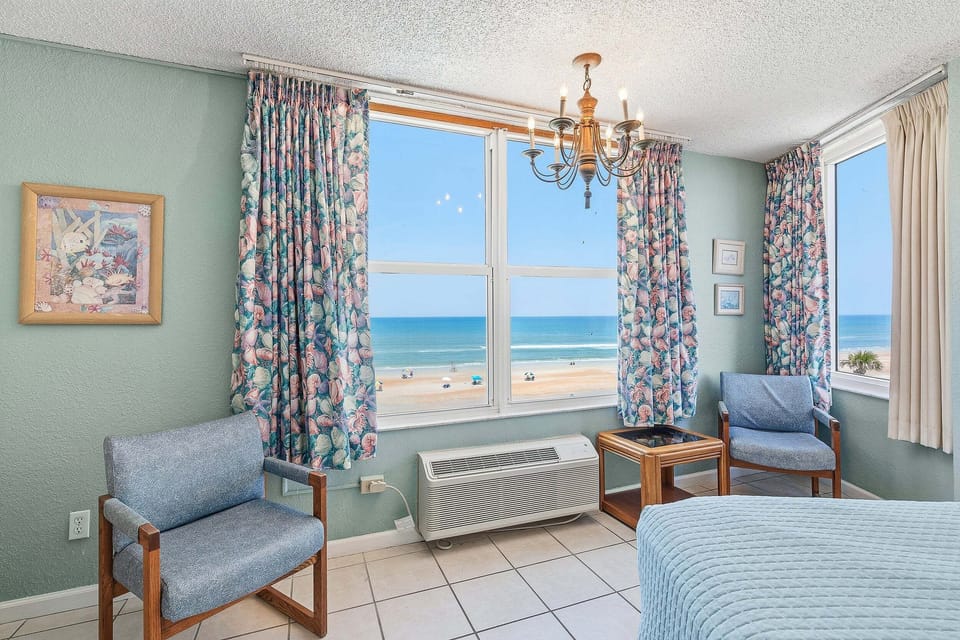 Wake up to sweeping ocean views from this bright beachfront bedroom featuring large windows, cozy seating, and coastal décor. The perfect beach stay retreat for enjoying stunning sunrises and the relaxing sights and sounds of the shore.