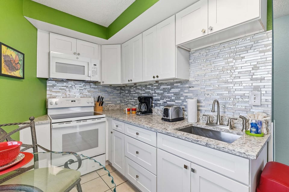Prepare meals with ease in this updated coastal kitchen featuring modern cabinetry, granite countertops, full-size appliances, and everything needed for a relaxing beach stay after a day by the ocean.