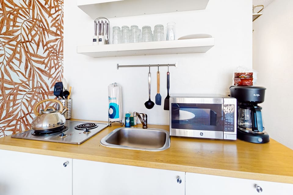 Bright beach-stay kitchenette featuring a cooktop, microwave, coffee maker, and essentials. Perfect for preparing quick seaside meals during your Daytona getaway.