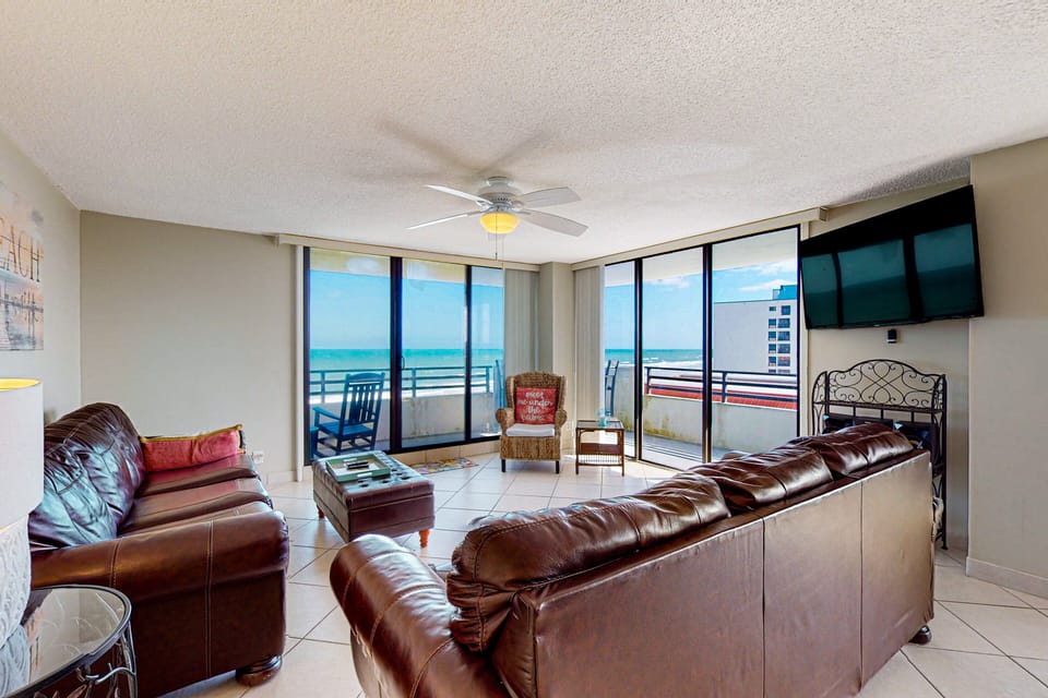 Spacious beach stay living room with wraparound ocean views, cozy leather seating, and floor-to-ceiling windows. Perfect for relaxing after a day on the sand and soaking in stunning coastal scenery.